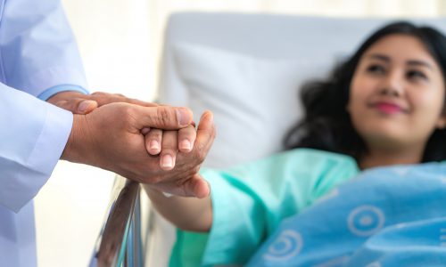 Friendly man doctor hands holding patient hand sitting at the de Friendly man doctor hands holding patient hand sitting at the desk for encouragement, empathy, cheering and support while medical examination. Bad news lessening, trust and ethics concept