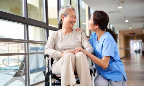 friendly staff caregiver of nursing home talking to asian senior woman in hallway