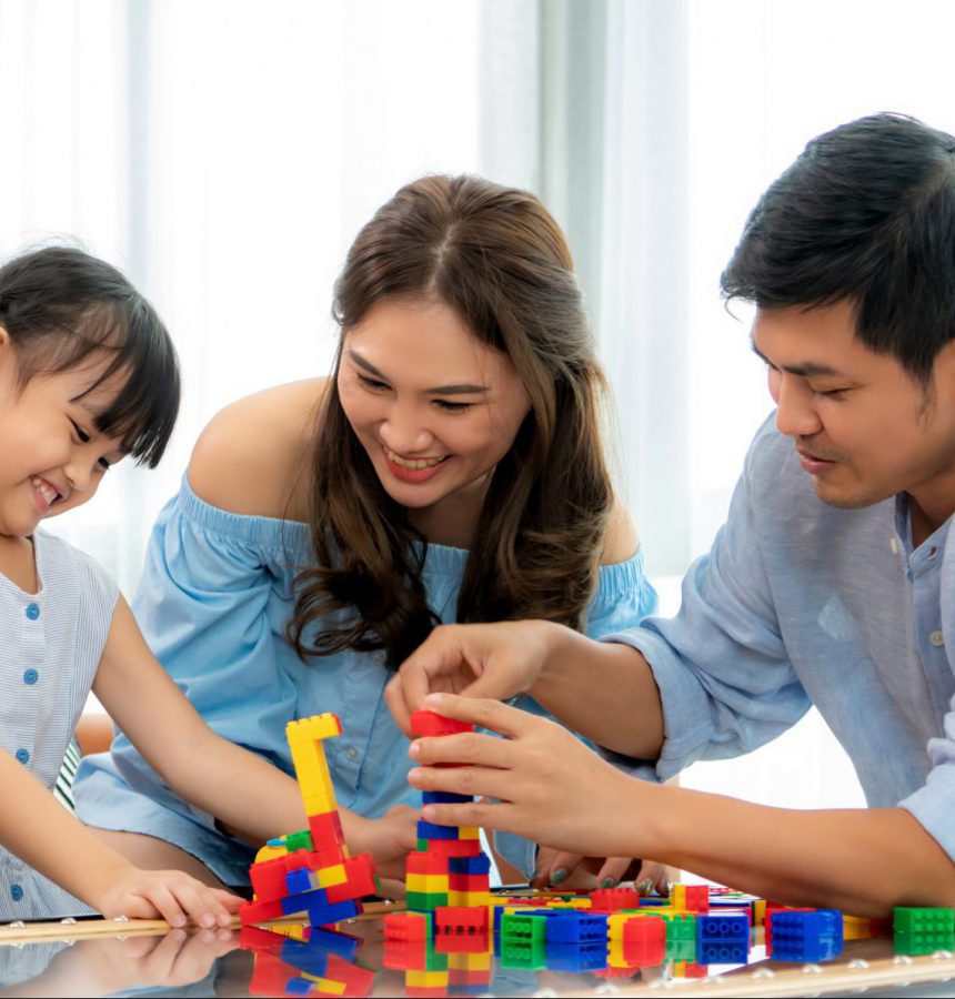 Asian family spends time in playroom with father, mother and daughter with toys on room background build out of plastic blocks in living room at home